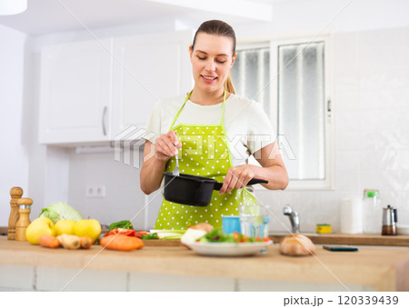 Woman in apron cooking delicious soup in pot in kitchen 120339439