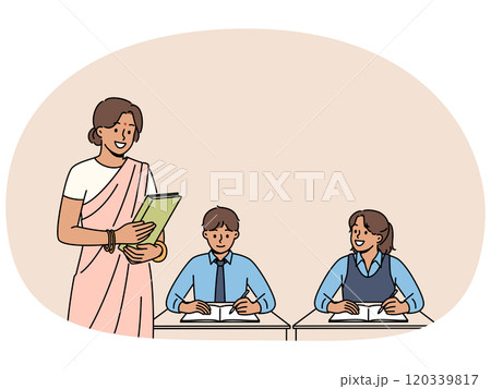 Indian woman teacher works in primary school, standing near children sitting at desks in classroom 120339817