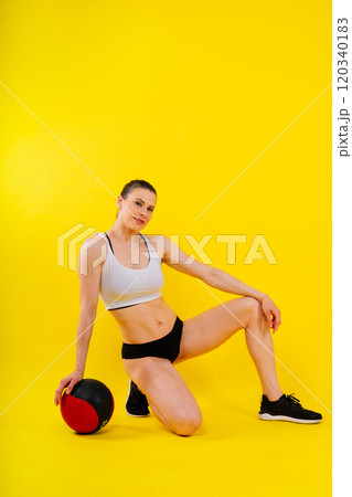 Sportive caucasian cross fit woman with fitness ball, look at camera. Studio dark yellow background 120340183