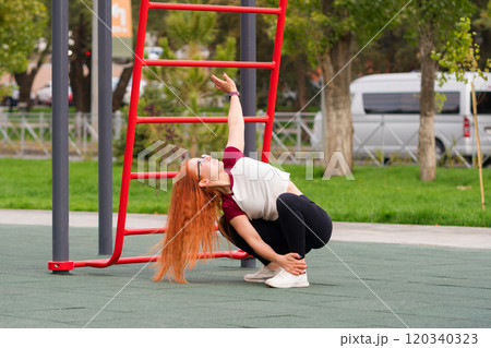 Woman stretching upward while squatting during outdoor exercise 120340323