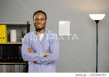 Successful black guy standing with crossed arms at his work place in the office Successful black guy standing with crossed arms at his work place in the office 120340355