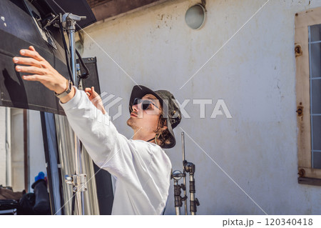 gaffer or the chief electrician in a motion-picture or television production unit set up the lights and light stand on a commercial shoot gaffer or the chief electrician in a motion-picture or television production unit set up the lights and light stand on a commercial shoot 120340418