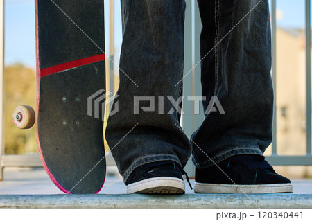 Skateboarder in baggy jeans holding scratched pink skateboard at city street. Teenager is skateboarding. Concept of youth subculture 120340441