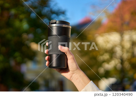 Woman holding reusable coffee cup on blurred autumn background. Concept of sustainable and eco-friendly living 120340490