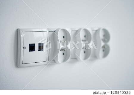 Close-up of white electrical sockets and ethernet ports on white wall 120340526