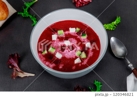 Vibrant bowl of beetroot soup features swirls cream cubes fresh vegetable dish is presented beautifully on dark table, surrounded by greens. Vibrant bowl of beetroot soup features swirls cream cubes fresh vegetable dish is presented beautifully on dark table, surrounded by greens. 120346821