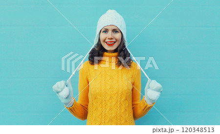 Winter christmas portrait of happy woman smiling in yellow sweater, white hat on blue background Winter christmas portrait of happy woman smiling in yellow sweater, white hat on blue background 120348513