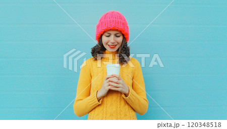 Happy smiling young woman with cup of coffee drink in winter hat, yellow sweater on blue background Happy smiling young woman with cup of coffee drink in winter hat, yellow sweater on blue background 120348518