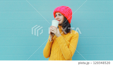 Happy smiling young woman with cup of coffee drink in winter hat, yellow sweater on blue background 120348520