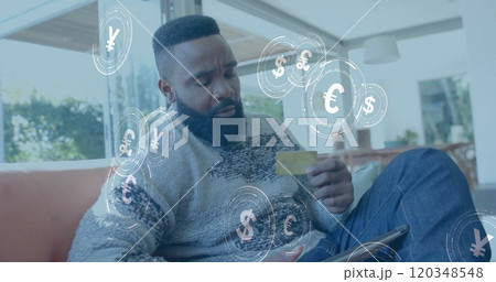 Image of currency icons and data over african american man paying online with card 120348548