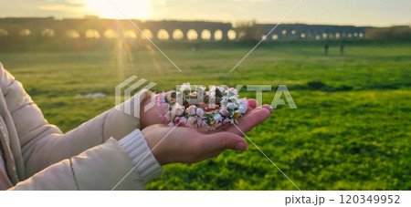 A delicate flower crown cradled in hands at sunset near an ancient aqueduct on a peaceful afternoon 120349952