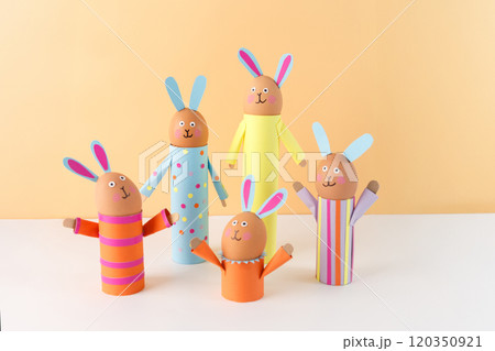 Handmade Easter bunny crafts using colored paper and eggs on a peach background. holder made of recycled toilet paper roll. Easter celebration and DIY craft concept. 120350921