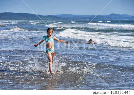 An 8 year old girl in a swimsuit having fun in the sea waves. An 8 year old girl in a swimsuit having fun in the sea waves. 120351444