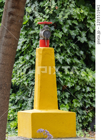 Ensuring fire safety, red hydrant on large concrete yellow pole, against backdrop of green foliage on grounds of hotel Ensuring fire safety, red hydrant on large concrete yellow pole, against backdrop of green foliage on grounds of hotel 120351941