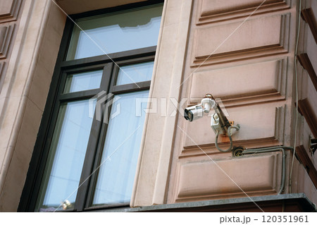From a highangle perspective, a security camera is mounted on a building next to the window to ensure safety and continuous monitoring to avoid robbery From a highangle perspective, a security camera is mounted on a building next to the window to ensure safety and continuous monitoring to avoid robbery 120351961