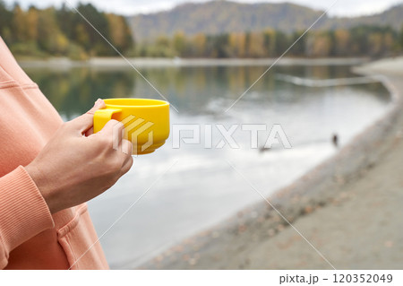 Relaxing morning by the lake: close up of hand holding yellow mug with tranquil Relaxing morning by the lake: close up of hand holding yellow mug with tranquil 120352049