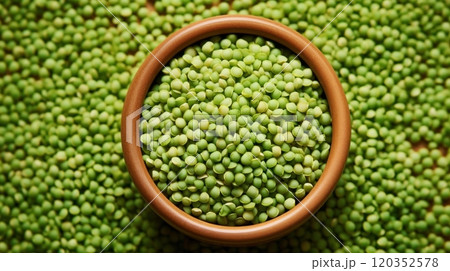 Close-up view of green lentils in a wooden bowl on a background of scattered lentils. Top view. Ideal for culinary and food-related content 120352578