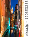 A narrow canal in Venice, Italy, at night, with a boat and a tall bell tower of St Mark's Campanile in the distance 120353238