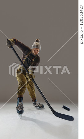 Man wearing pants with suspenders, knitted warm sweater and hat, in motion with stick, hitting puck. Winter sports and activity 120353427