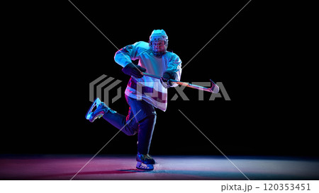 Competitive man, hockey player wearing full game gear, in motion with stick, competing for the victory against black studio background in neon light Competitive man, hockey player wearing full game gear, in motion with stick, competing for the victory against black studio background in neon light 120353451