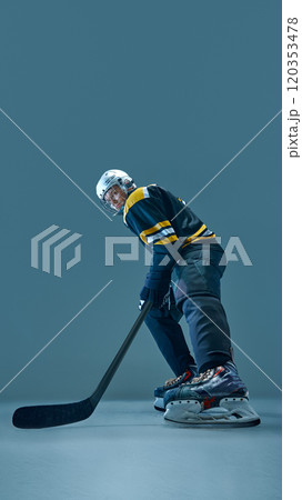 Vertical full-length image of concentrated man, hockey player in helmet and uniform, standing with stick, preparing for intensive game 120353478