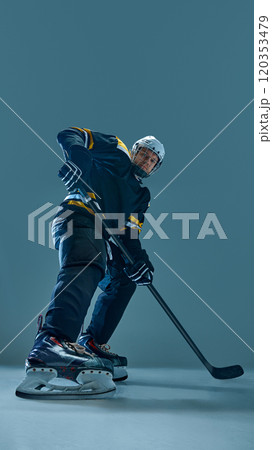 Vertical full-length image of concentrated man, hockey player in helmet and uniform, standing with stick, preparing for intensive game 120353479