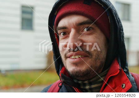 A cheerful man stands outdoors in winter attire, his hood pulled up and a beanie snug on his head, radiating warmth and joy in a cold environment. 120354920
