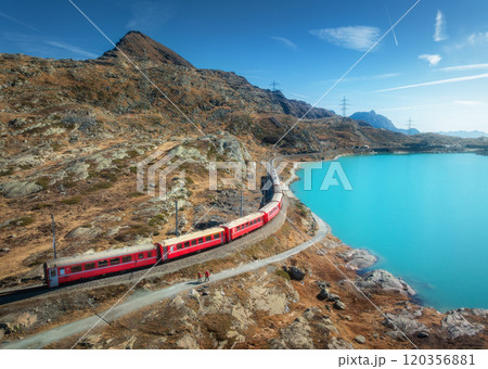 Aerial view of red train near azure mountain lake, snowy rocks 120356881