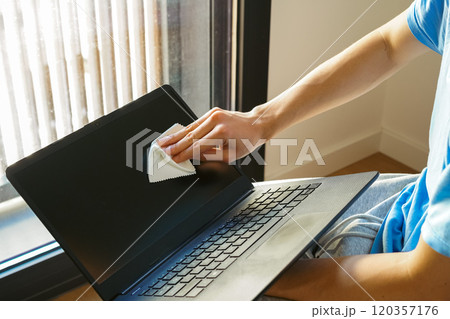 パソコンのモニターをクリーニングクロスで掃除する若い男性 120357176