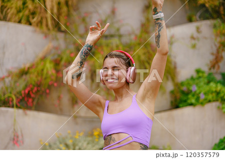 A Joyful Woman is Dancing Outdoors While Wearing Headphones in a Bright, Sunny Setting 120357579