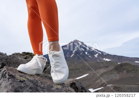 Close-up unrecognizable legs belonging to female fitness model. Fit woman wearing orange skintight gym leggings, sneakers while hiking and trail running. Part of fitness training session in mountains 120358217