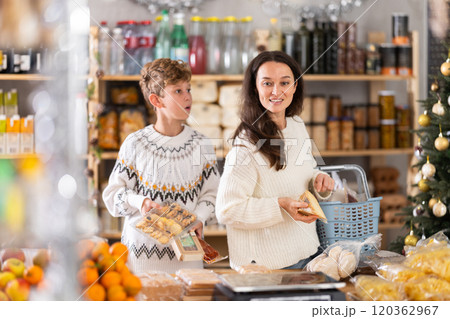 Adolescence boy with mother choose consider snacks in shop on eve of New Year Adolescence boy with mother choose consider snacks in shop on eve of New Year 120362967