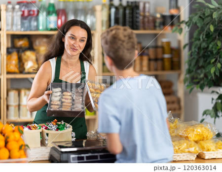Female seller offers to buy cookies to teenage boy in interior of grocery supermarket Female seller offers to buy cookies to teenage boy in interior of grocery supermarket 120363014