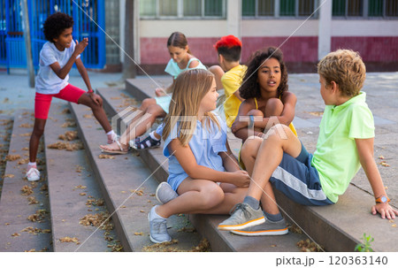 Positive tweenagers friendly blabbing while sitting on steps outdoors 120363140