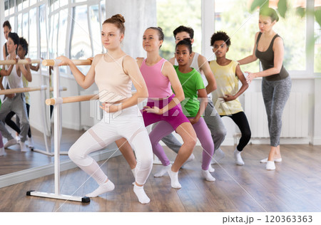 Teenage girl learning grand plie at barre at group ballet class 120363363