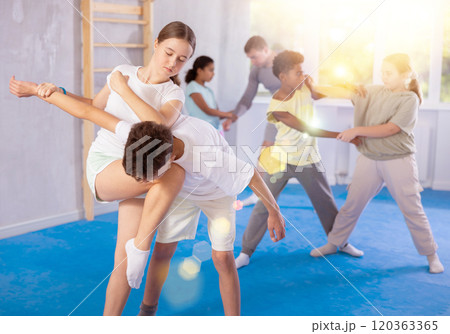 Tween girl applying armlock with elbow and knee blows to boy in mock bout at self-defense training 120363365