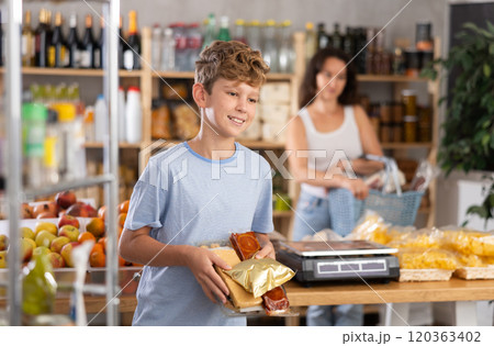 Joyful teenage boy choosing and buying different candies and sweets in supermarket 120363402