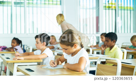 Focused tween schoolgirl writing in workbook during lesson 120363655