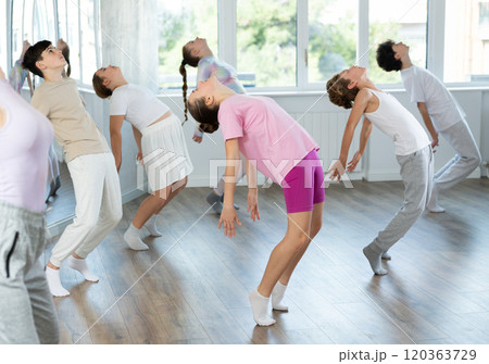 Female girl student repeats movements of unrecognizable teacher during group modern dance class. 120363729