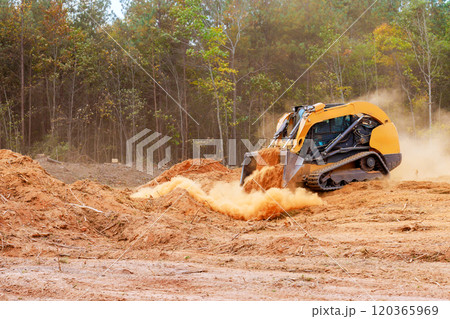Powerful bulldozer is actively pushing dirt debris at construction site surrounded by trees dust clouds billow into air as land is being prepared for development. 120365969
