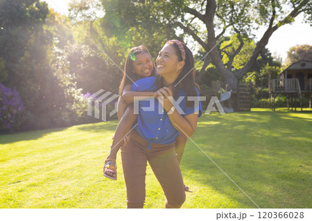 Giving daughter piggyback ride, mother smiling and enjoying sunlight in backyard Giving daughter piggyback ride, mother smiling and enjoying sunlight in backyard 120366028
