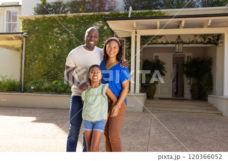 Smiling family of three with daughter standing together outside their home, enjoying time Smiling family of three with daughter standing together outside their home, enjoying time 120366052