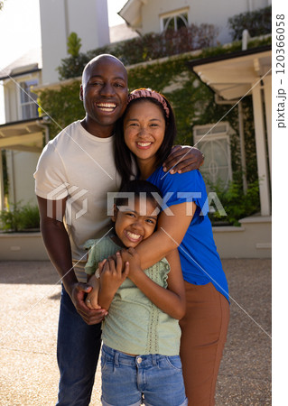 Smiling family of three with daughter hugging and posing outside their home 120366058