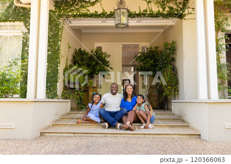 Sitting on porch steps, happy family of four with daughters smiling and enjoying time together 120366063