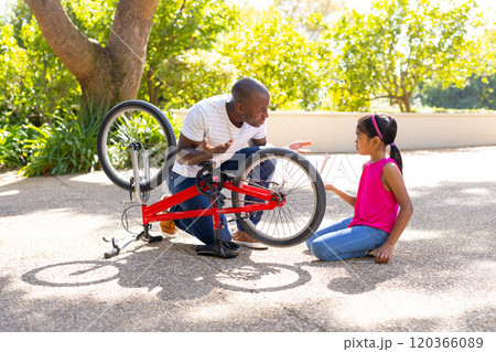 Father teaching daughter bicycle maintenance skills outdoors, fixing bike together Father teaching daughter bicycle maintenance skills outdoors, fixing bike together 120366089