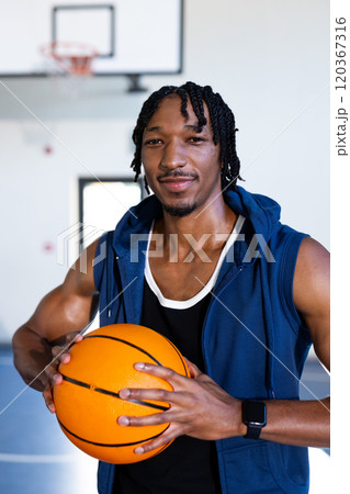 Holding basketball, african american man smiling confidently in indoor school basketball court 120367316