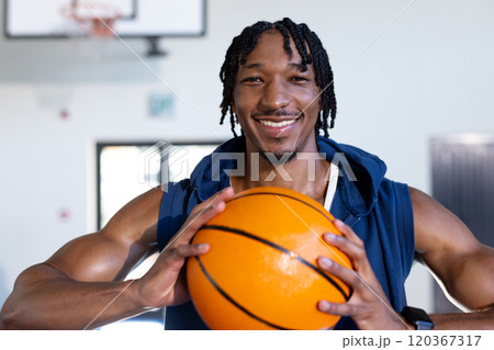 Holding basketball, smiling african american man posing confidently in indoor gym court 120367317