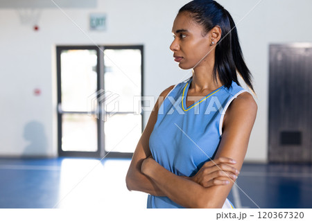 Female basketball player standing with arms crossed, looking determined in gym, copy space 120367320
