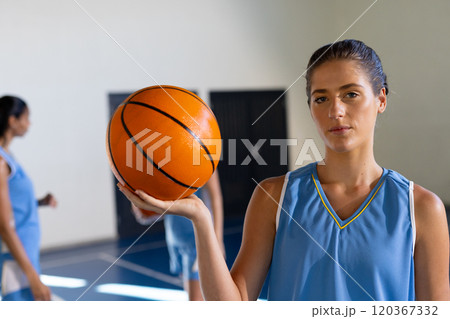 Holding basketball, female athlete in uniform standing on indoor court 120367332