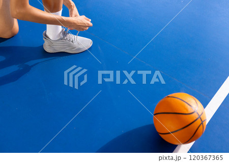 Tying shoelaces on basketball court, woman preparing for game with ball nearby, copy space 120367365